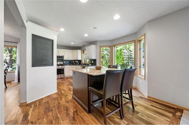 kitchen featuring decorative backsplash, white cabinets, wood finished floors, and stainless steel appliances