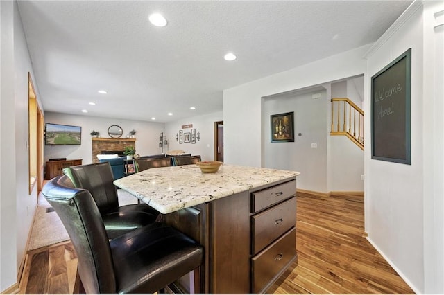 kitchen featuring wood finished floors, recessed lighting, a fireplace, a kitchen breakfast bar, and a center island