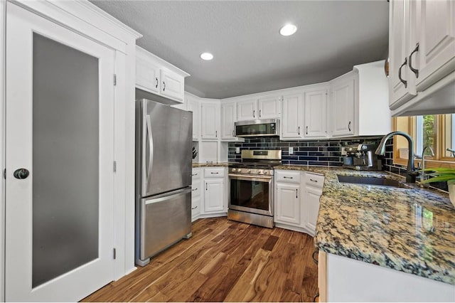 kitchen featuring tasteful backsplash, dark wood finished floors, appliances with stainless steel finishes, white cabinetry, and a sink