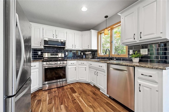 kitchen featuring dark wood-style floors, a sink, stainless steel appliances, white cabinetry, and backsplash