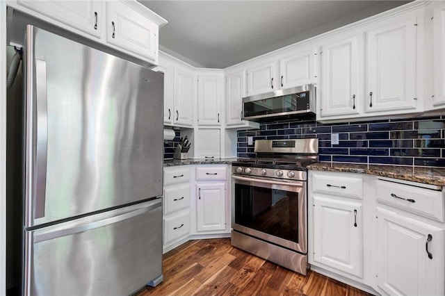 kitchen with dark stone countertops, dark wood finished floors, appliances with stainless steel finishes, white cabinets, and decorative backsplash