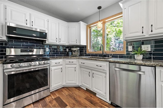 kitchen with a sink, dark wood-type flooring, appliances with stainless steel finishes, white cabinetry, and backsplash