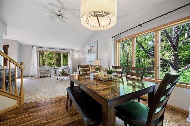 dining space with baseboards, stairs, vaulted ceiling, ceiling fan with notable chandelier, and wood finished floors