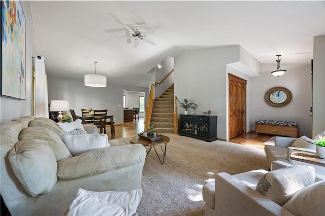 living room featuring lofted ceiling, stairway, carpet flooring, and ceiling fan