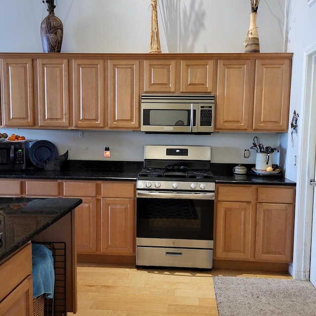 kitchen featuring brown cabinetry, dark stone counters, stainless steel appliances, and light wood-style floors