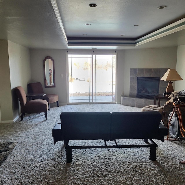 living area featuring a raised ceiling, carpet flooring, baseboards, and a tile fireplace