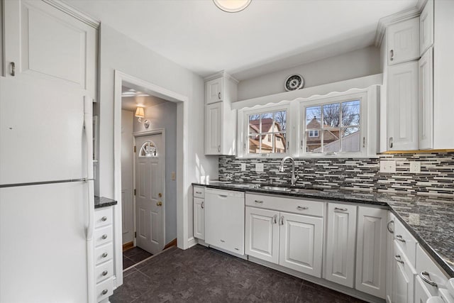 kitchen with white appliances, dark stone counters, a sink, decorative backsplash, and white cabinets