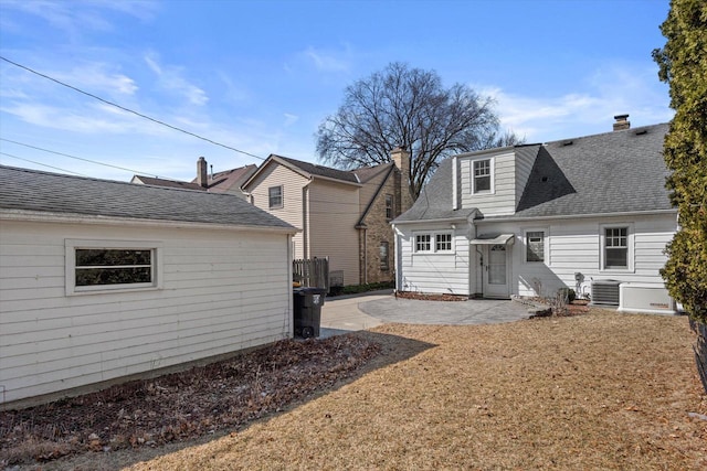 back of house featuring a lawn, cooling unit, a shingled roof, and a patio