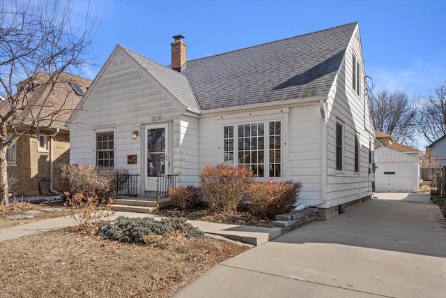 view of front of property with an outbuilding, a chimney, a detached garage, and a shingled roof