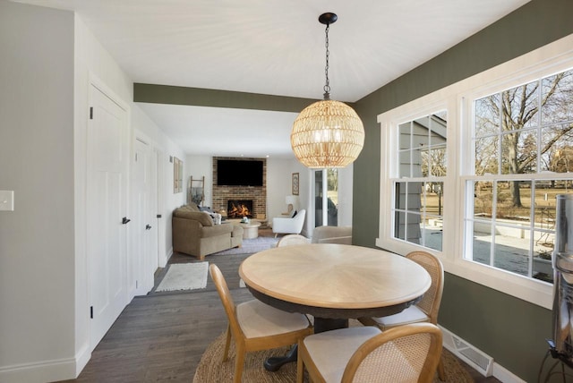 dining area featuring dark wood-style floors, visible vents, baseboards, a fireplace, and a notable chandelier