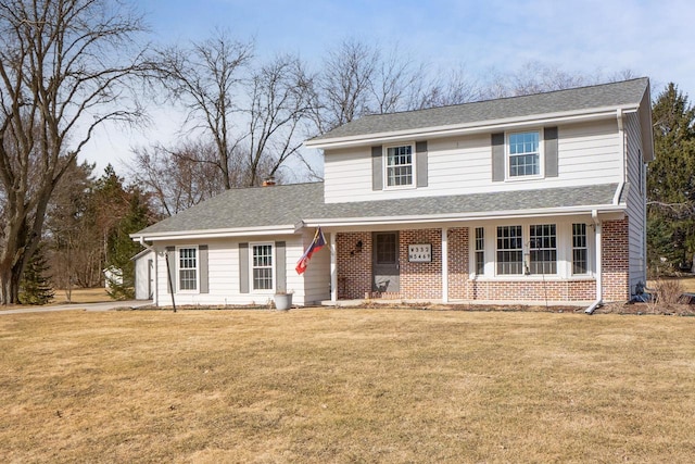 traditional-style home with brick siding, covered porch, a shingled roof, and a front lawn