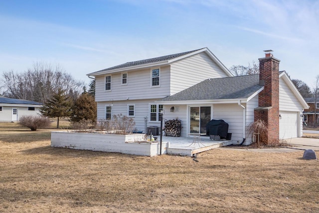 back of property featuring a yard, a chimney, an attached garage, and a shingled roof