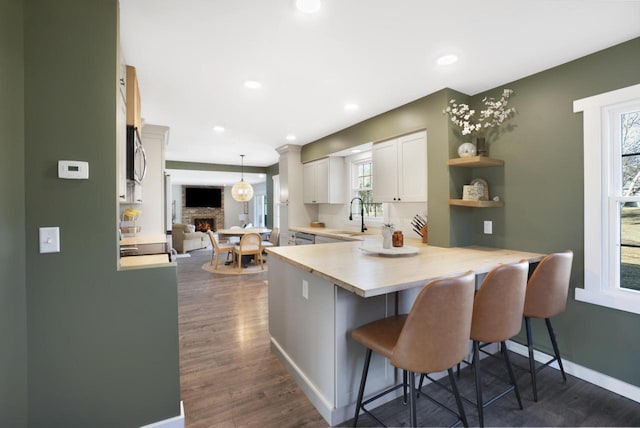 kitchen featuring a sink, a kitchen breakfast bar, dark wood-style floors, a peninsula, and light countertops