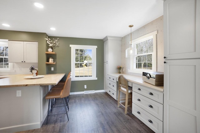 kitchen featuring open shelves, dark wood finished floors, built in desk, recessed lighting, and a breakfast bar area