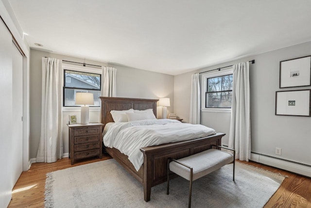 bedroom with light wood-style flooring, a baseboard heating unit, and baseboards