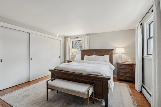 bedroom with a baseboard radiator, light wood-style floors, and a closet