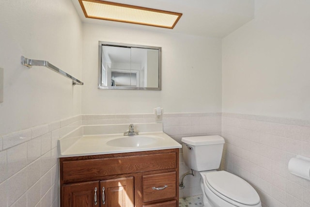 bathroom with wainscoting, toilet, vanity, and tile walls