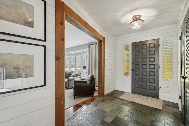 entrance foyer featuring stone tile flooring, ornamental molding, and wood walls