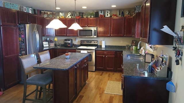 kitchen featuring a sink, appliances with stainless steel finishes, a kitchen bar, light wood-type flooring, and reddish brown cabinets