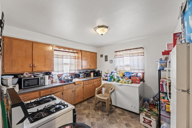 kitchen featuring stainless steel microwave, stone finish floor, brown cabinets, and gas range gas stove