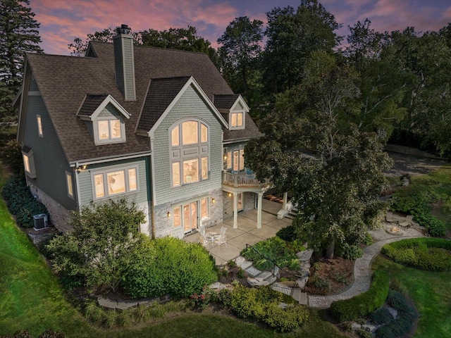 back of house with central AC unit, a shingled roof, a chimney, and a patio area