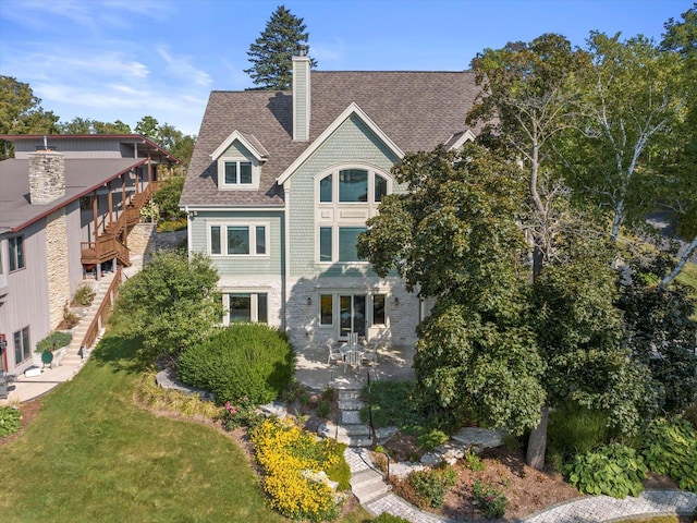 view of front of home featuring stairway, roof with shingles, a front yard, a chimney, and a patio area