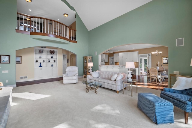 carpeted living area with built in features, visible vents, arched walkways, and an inviting chandelier