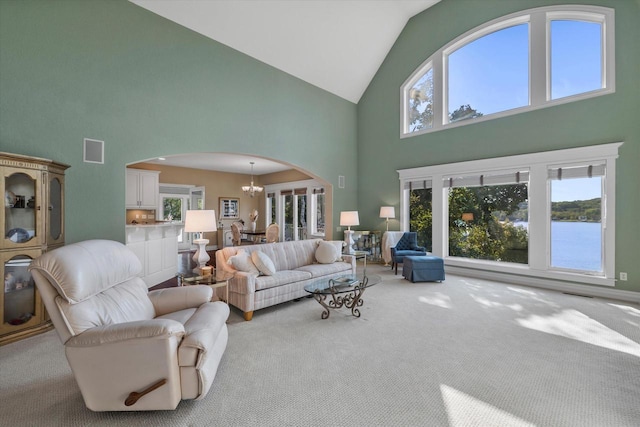 carpeted living room with an inviting chandelier, visible vents, arched walkways, and lofted ceiling