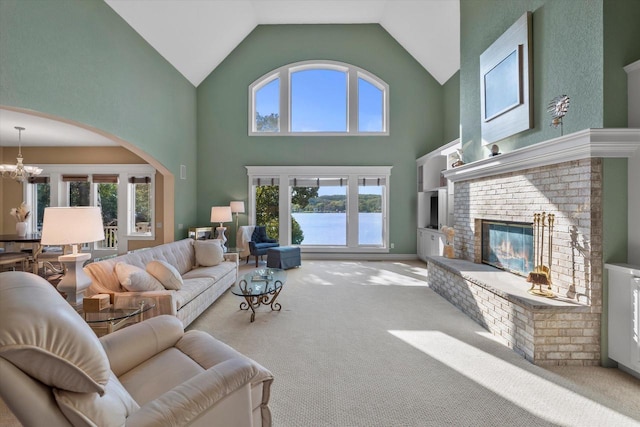 carpeted living area featuring an inviting chandelier, a brick fireplace, a water view, and a wealth of natural light