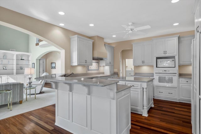 kitchen featuring white appliances, custom range hood, arched walkways, and dark wood-type flooring