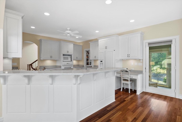 kitchen with white appliances, dark wood-style floors, a peninsula, recessed lighting, and a kitchen bar