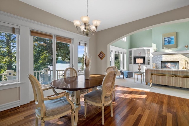 dining room with visible vents, a fireplace, an inviting chandelier, wood finished floors, and arched walkways