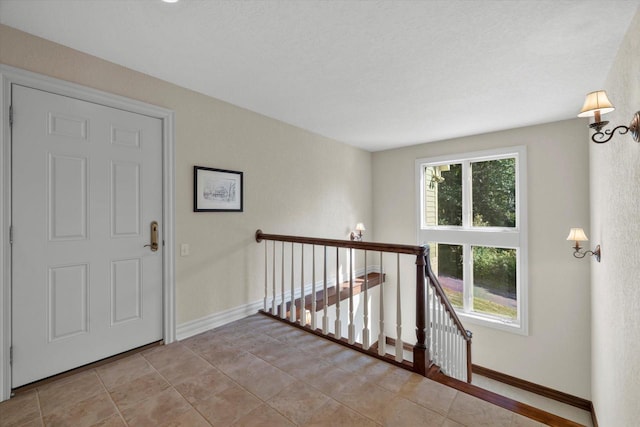 hall with light tile patterned floors, baseboards, and an upstairs landing