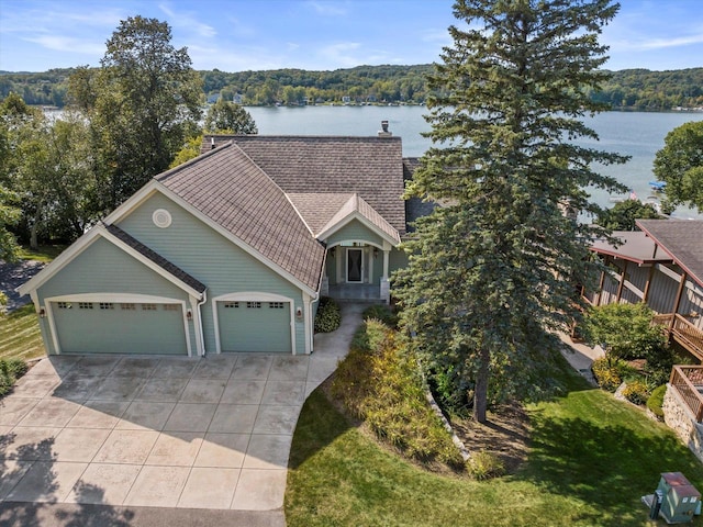 view of front of home with roof with shingles, driveway, a chimney, a water view, and a garage