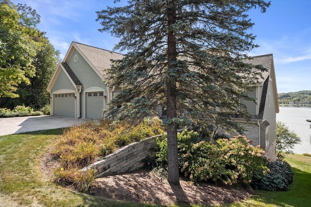 view of property exterior with roof with shingles, an attached garage, a yard, concrete driveway, and a water view