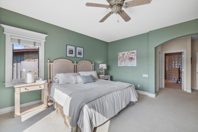 carpeted bedroom featuring arched walkways, a ceiling fan, and baseboards