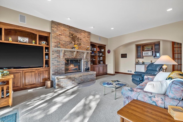 living room featuring visible vents, a brick fireplace, built in shelves, carpet flooring, and arched walkways