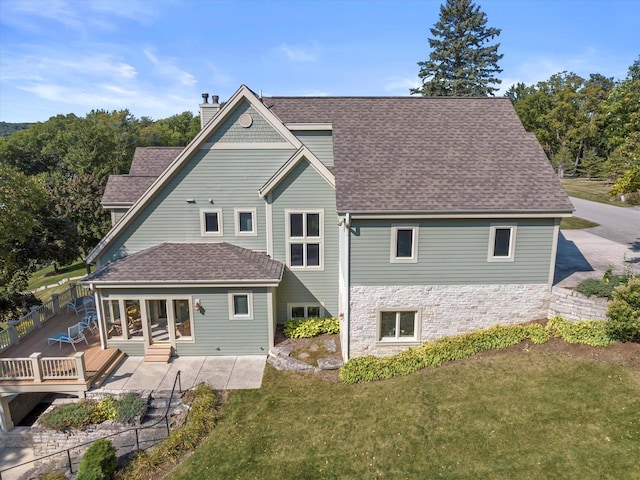 back of property featuring fence, a yard, a chimney, a shingled roof, and stone siding