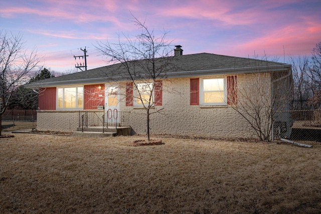 single story home with a shingled roof, a lawn, brick siding, and a chimney