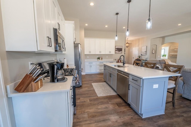 kitchen with a sink, a kitchen breakfast bar, dark wood-style floors, arched walkways, and appliances with stainless steel finishes