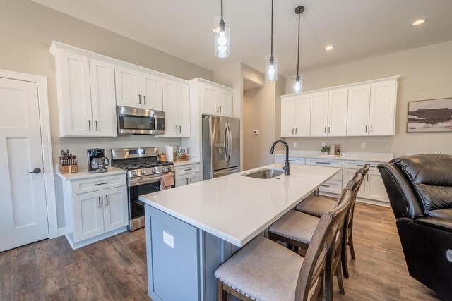 kitchen with a sink, a kitchen bar, light countertops, stainless steel appliances, and dark wood-style flooring