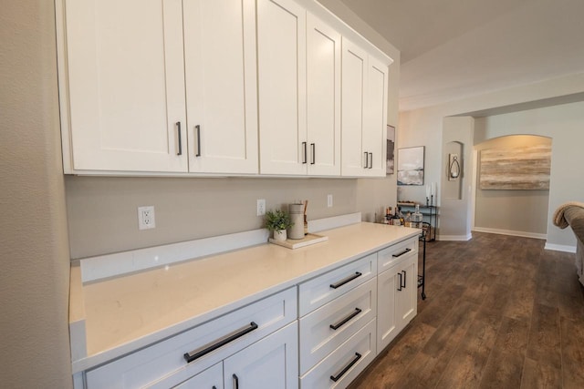 kitchen with baseboards, light countertops, arched walkways, white cabinetry, and dark wood-style flooring