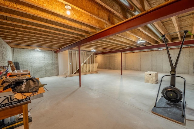 unfinished basement featuring stairs and brick wall