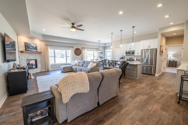 living room with a ceiling fan, dark wood-style floors, recessed lighting, a stone fireplace, and baseboards