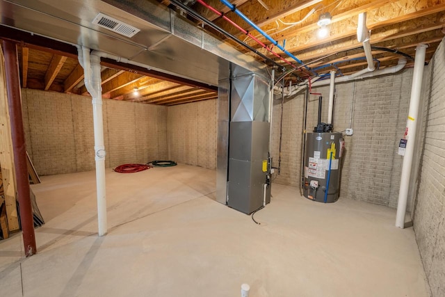 unfinished basement featuring heating unit, visible vents, gas water heater, and brick wall