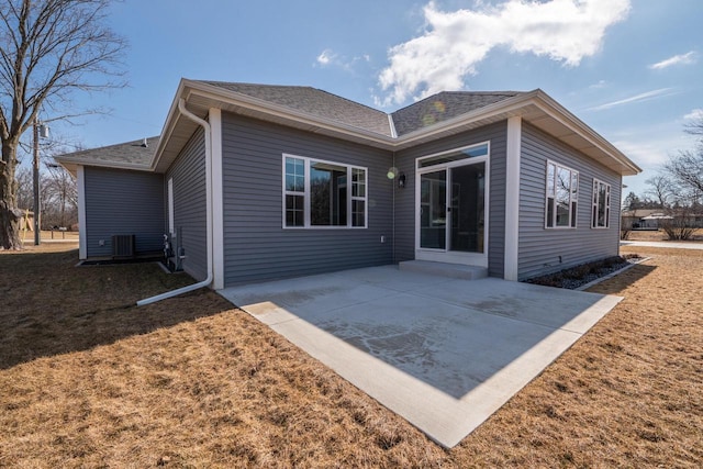 rear view of property featuring central air condition unit, a lawn, a patio, and roof with shingles