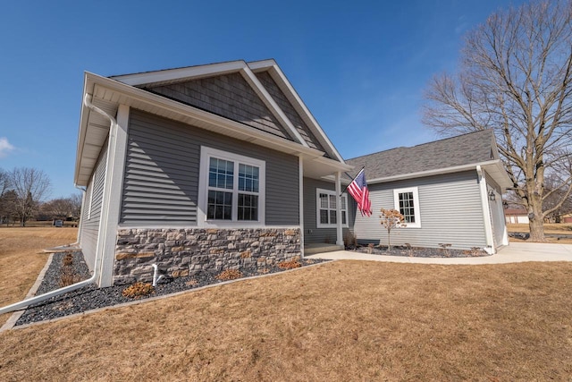 view of front of property featuring stone siding, roof with shingles, and a front lawn