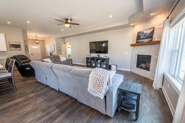 living area featuring a stone fireplace, dark wood finished floors, arched walkways, and a healthy amount of sunlight