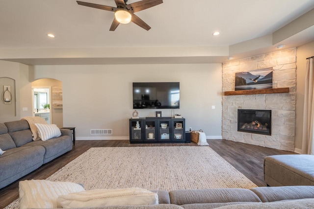 living area featuring arched walkways, visible vents, a stone fireplace, and wood finished floors