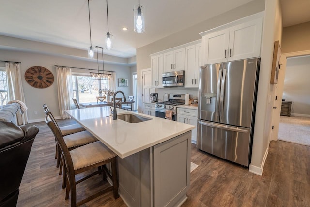 kitchen featuring a kitchen island with sink, a sink, appliances with stainless steel finishes, a breakfast bar area, and white cabinets